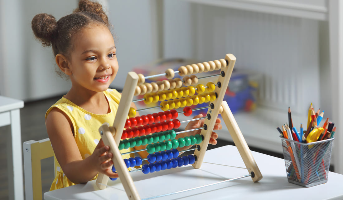 Smiling young girl using a colorful abacus at a classroom desk