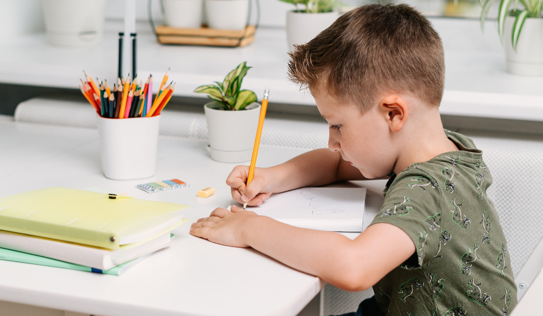A young boy is focused on writing on a piece of paper at a table, with a pencil in hand.