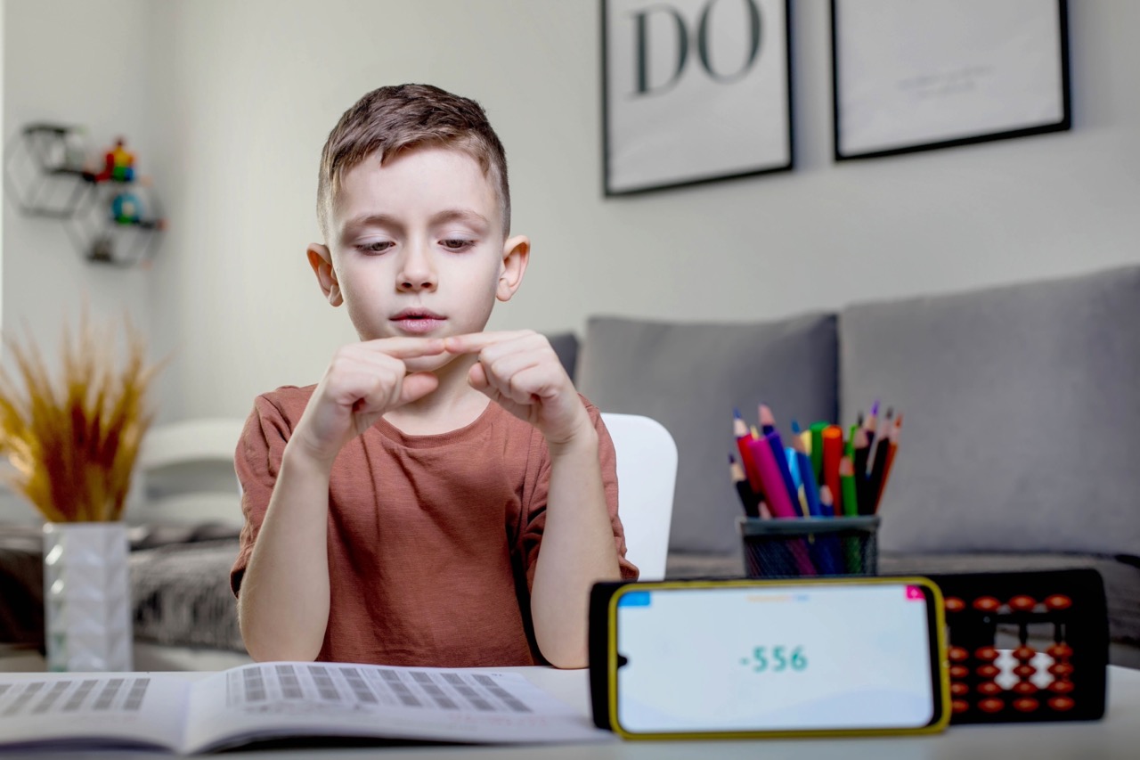 A boy counts on fingers with an exercise book open in front of him.