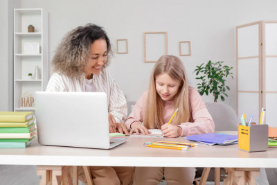 A mother and daughter sit side by side, focused on a laptop, working together on a project or task.