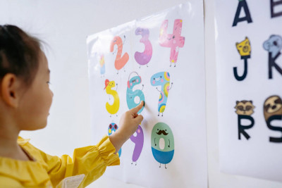 A young girl is pointing at a poster that features a series of numbers, showcasing her curiosity and engagement.
