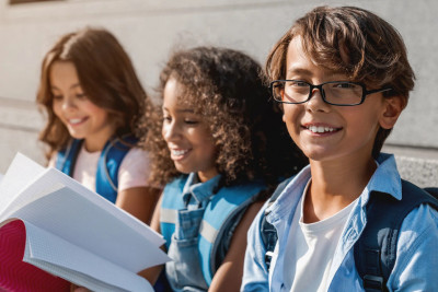Three bespectacled children are seated on a bench, displaying cheerful expressions as they interact with one another.