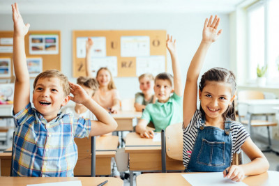 A classroom scene with children eagerly raising their hands to answer questions, showcasing engagement and participation.