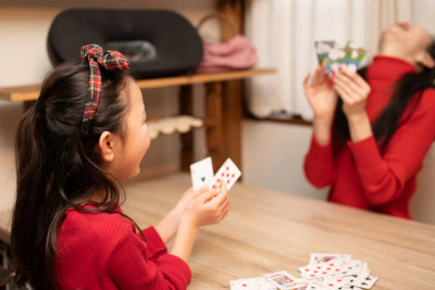 A young girl and her mother sit at a table, smiling and playing cards together in a cozy indoor setting.