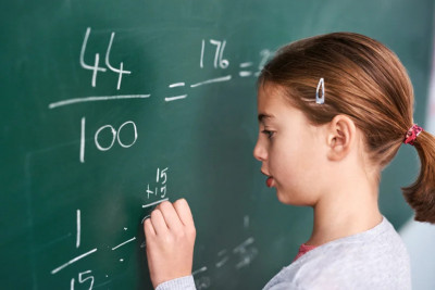 A young girl using chalk to write numbers on a blackboard, demonstrating her learning process.