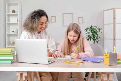 A woman and a girl are seated at a table, engaged in an activity using a laptop.