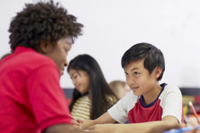 A group of children attentively sitting at desks in a bright classroom, engaged in learning activities.