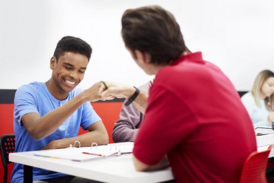 A tutor and a student at a table, shaking hands, representing a positive interaction between them.