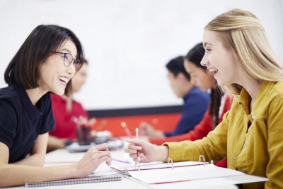 A math tutor and a student engage in discussion at a classroom desk, surrounded by books and learning materials.
