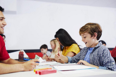 A math tutor interacts with a student at a table, fostering a collaborative learning environment.